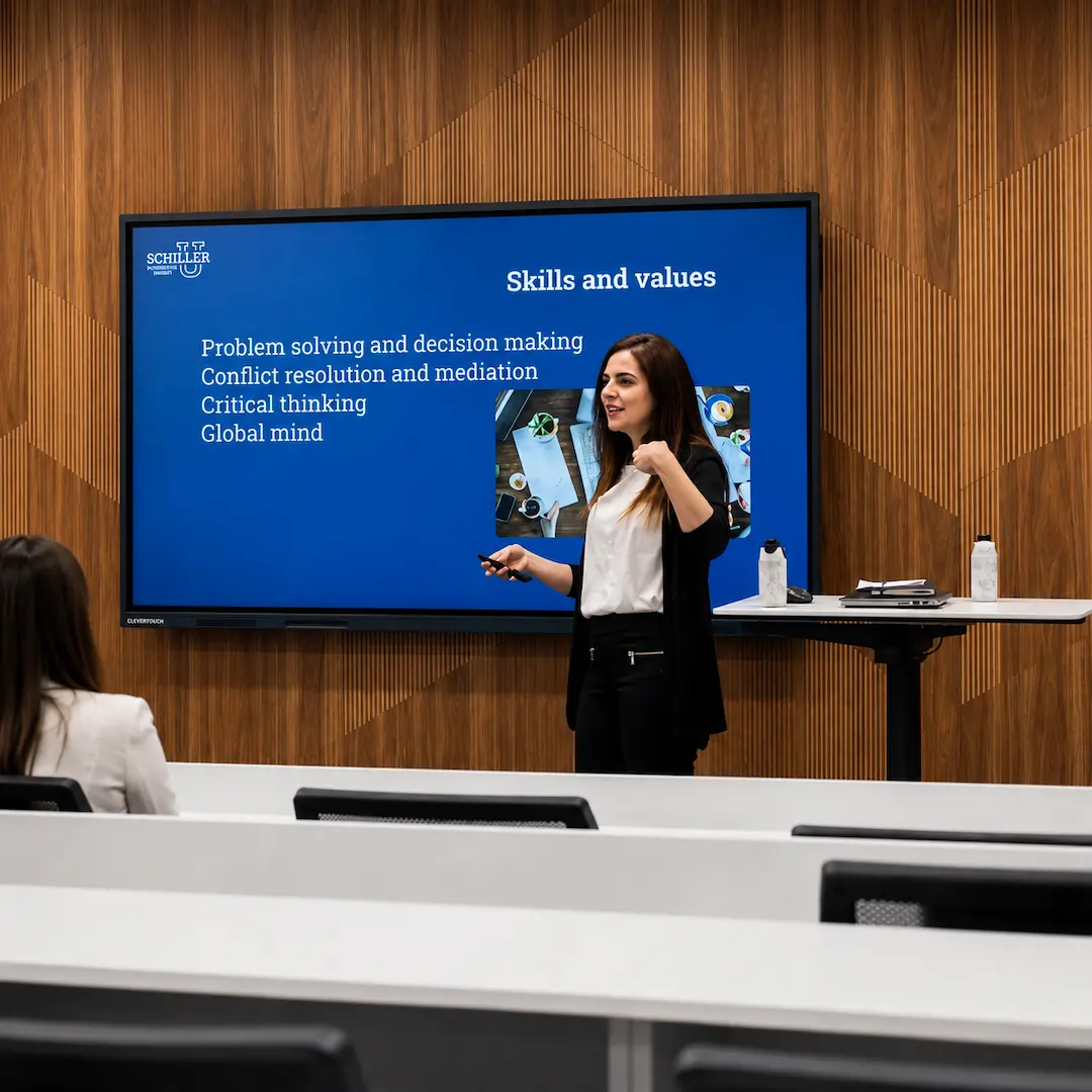Miriam Jiménez, Associate Dean of International Relations and Diplomacy at Schiller International University, stands in front of a digital whiteboard in a classroom